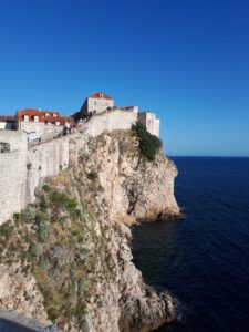Auf der linken Seite im Bild sieht man die hohe Stadtmauer von Dubrovnik und die steile Steinküste zum Meer hin.