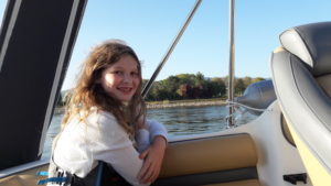 Auf diesem Foto sieht man die älteste Tochter der Familie. Sie sitzt auf der Rücksitzbank des Bootes und lächt in die Kamera.