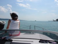 Fau S. sitzt vorne auf dem Bug der 20 -Yachtline-. Sie trägt ein pinke kurze Hose, ein weißes Top und einen schwarzen Sonnenhut. Sie genießt die Sonne an Deck. Das Foto wurde vom Fahrerstand aus gemacht und man hat so guten Blick auf das blau Wasser des Bodensees.