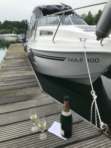 Die 23 -Yachtline- liegt am am Holzsteg des heimischen Bootsclub. Das Camperverdeck ist aufgebaut und vor dem Boot seht eine Flasche Sekt mit zwei Gläsern.