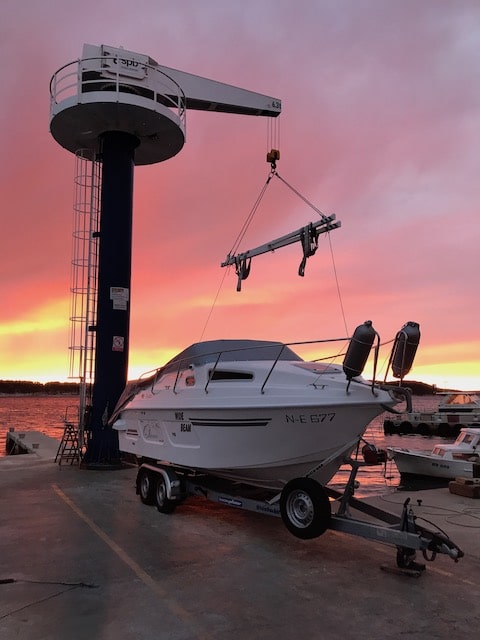 Die 23 -Yachtline- steht auf ihrem Trailer im Hafen, die Sonne geht gerade unter und der Himmel färbt sich in gelb, lila rosa Töne.