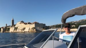 Herr E. steht stolz am Steuer seiner 23 -Yachtline-, im Hintergrund sieht man eine Kroatische Stadt und das Meer.