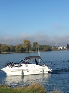 Das Foto wurde vom Ufer des Bodensee's gemacht, Herr B. steuert das boot an der Reling sind Klappfahrräder befestigt und das Camperverdeck ist auf gebaut hinter der 23 schwimmt ein Schwarm Blässhühner.