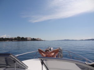Blick vom Fahrerstand aus nach vorne über das Boot hier liegt Herr H. auf dem Bug in blauer Badehose sonnt sich und lässt die Seele baumeln. Im Hintergrund sie man das Kroatischefestland.