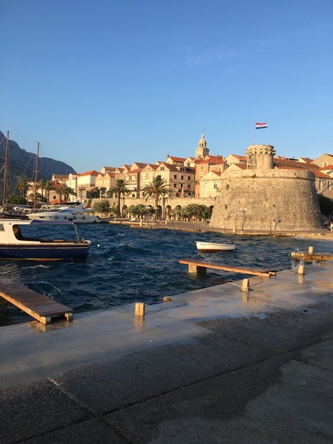 Das Foto zeigt den Hafen und die Stadtmauern von Dubrovnik, ein Boot fährt gerade aus dem Hafen.