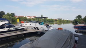 Die SR30 -Yachtline- ist im Hafen an eine Steg festgemacht vor ihr liegen andere Sportboote. Ihm Hintergrund sieht man das Ufer des Main's und die Häuser des angrenzenden Örtchens.