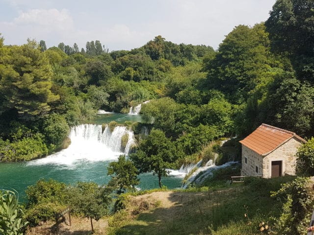 Idyllisch gelegen die Wasserfälle Krka, mit kleinem Steinhaus im Vordergrund.