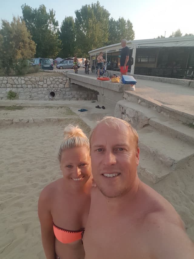 Herr & Frau H. lächeln in die Kamera (Selfi). Es ist der letzte Tag vor der Abreise am Strand, die Sonne geht bald unter.