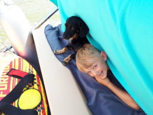Das Bild zeigt den jüngsten Sohn der Familie und den Dackel, sie liegen auf dem Bauch auf der hinteren Liegefläche der SR30 -Yachtline- eine türkise Deck hängt von oben herunter so das man nur die Köpfe der beiden sieht.