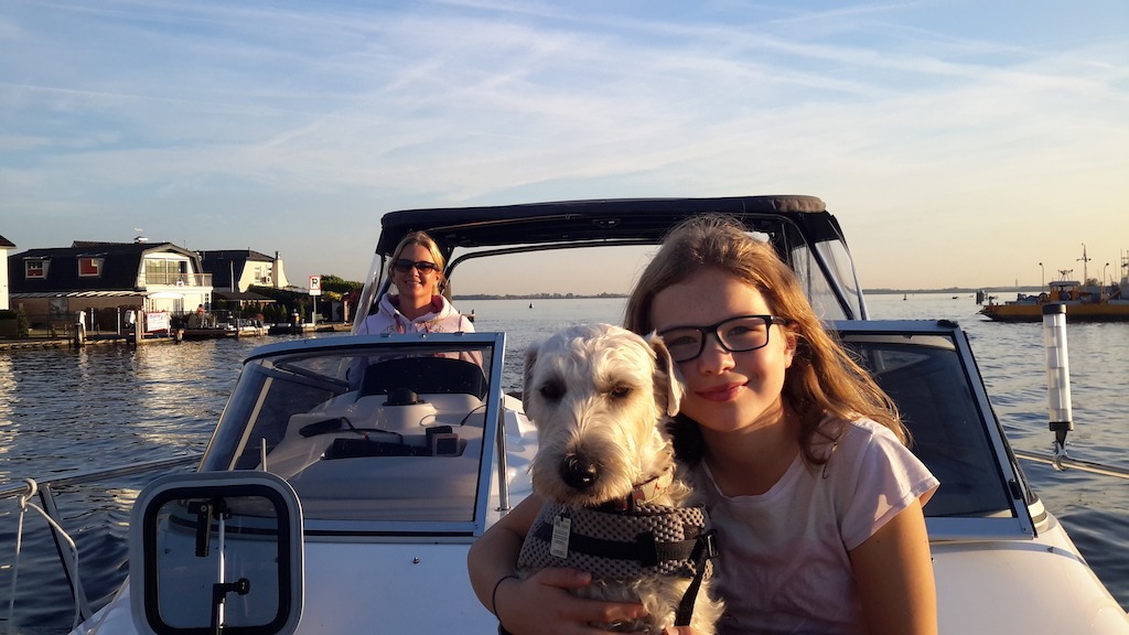 Das Foto wurde vom Bug aus gemacht Frau T. steht am Fahrerstand und steuert das Boot vorne auf der Liegefläche sitzt die jüngste Tochter der Familie mit ihrem und im Arm und lächelt in die Kamera.